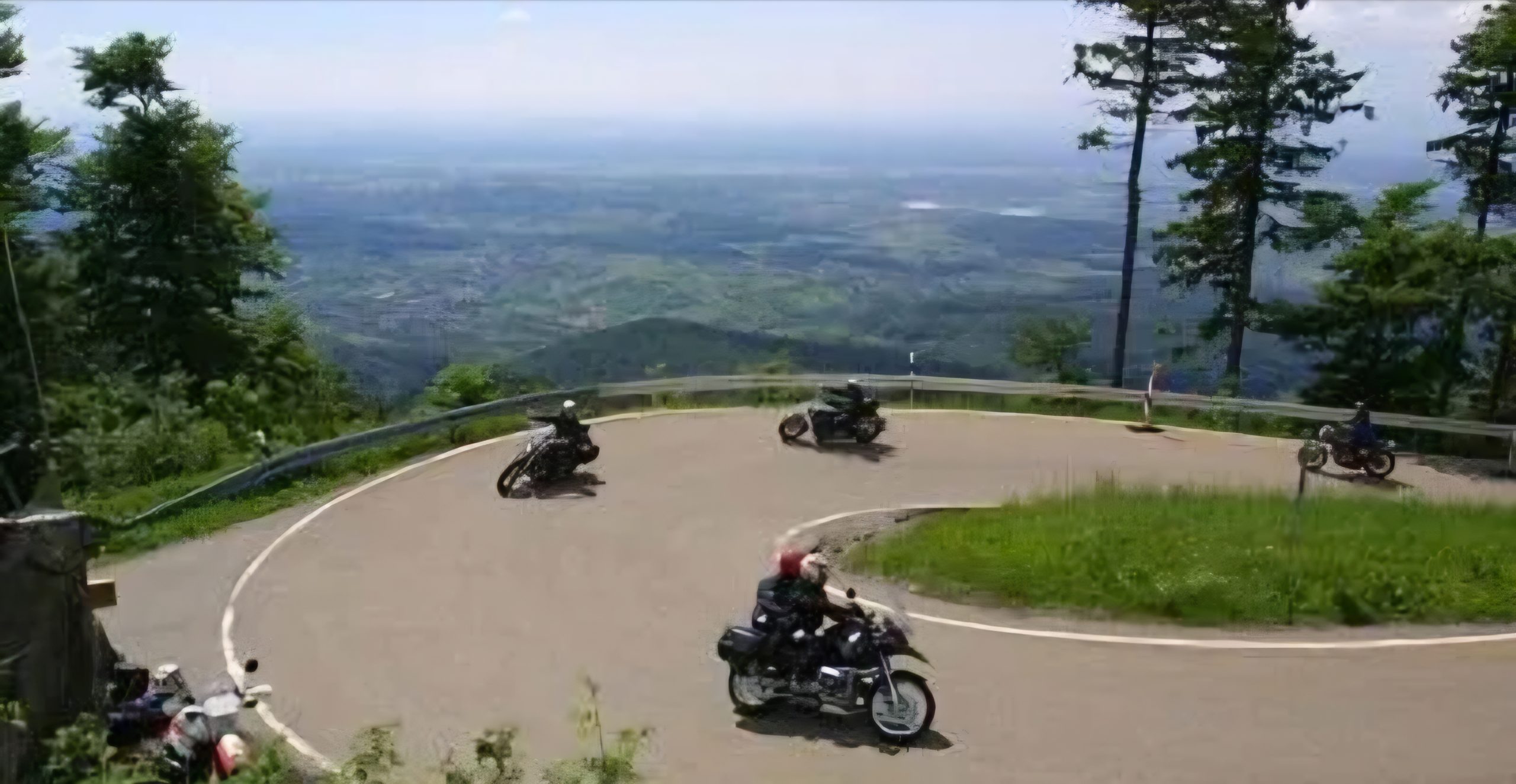 Motorrijders rijden door een steile haarspeldbocht met uitzicht over de Luxemburgse bergen tijdens een motortourtocht